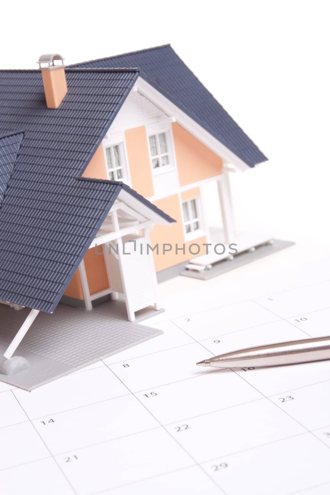 Moving house planning concept. Model of house situated on calendar. Focused on pen.