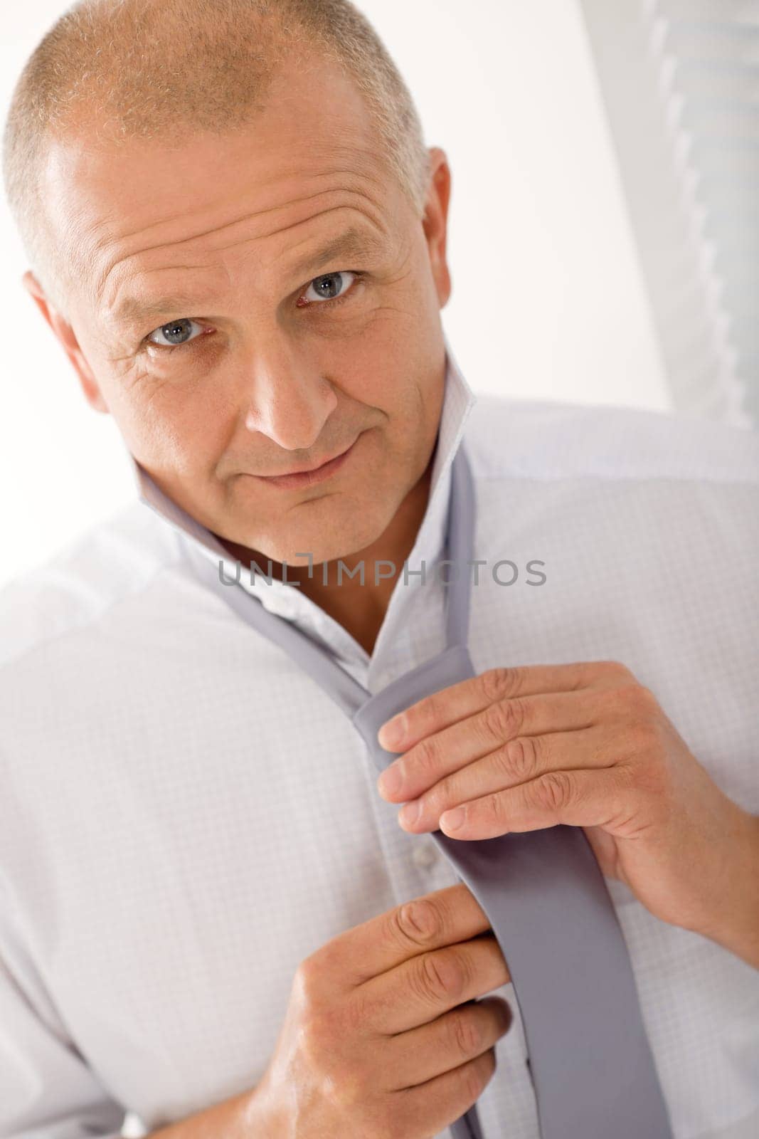 Handsome stylish mature business man smiling tie a tie closeup