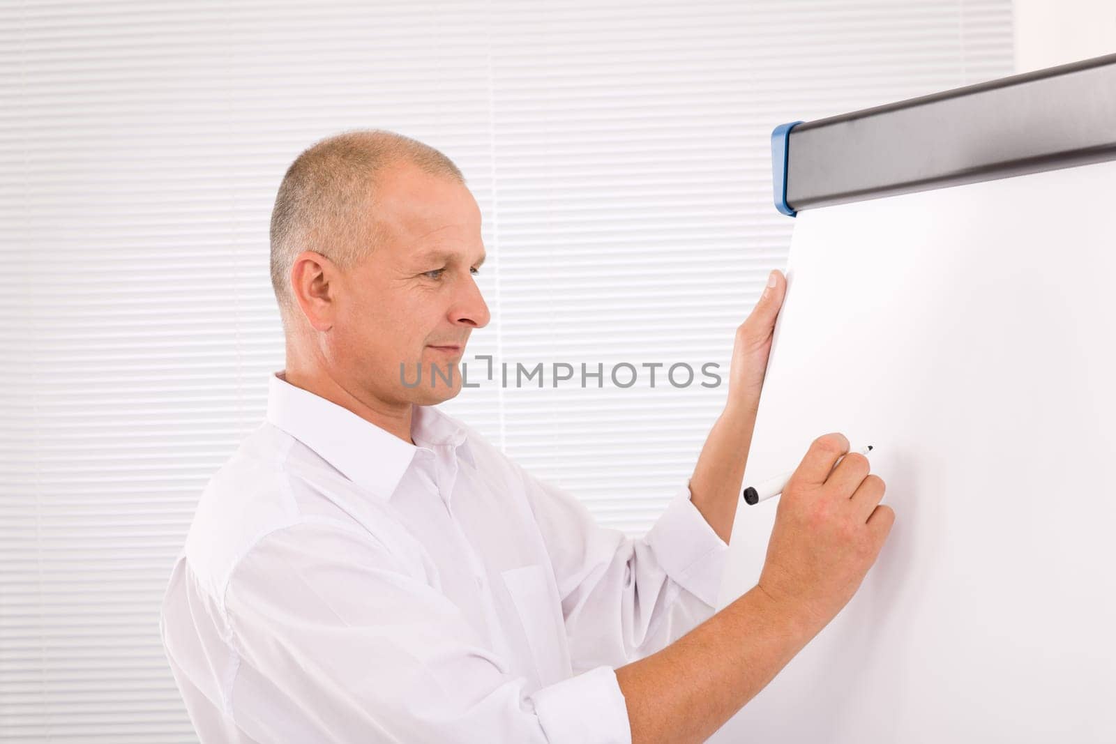Handsome mature businessman writing at empty flip chart looking aside