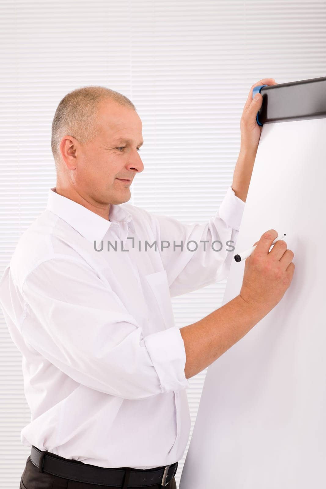 Handsome mature businessman writing at empty flip chart looking aside