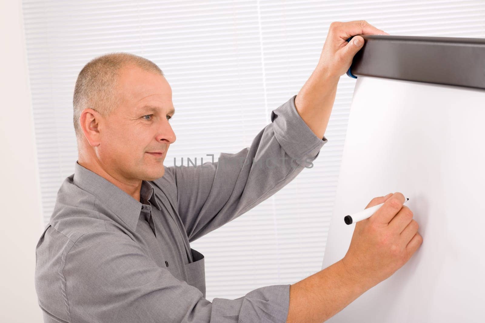 Handsome mature businessman writing at empty flip chart looking aside