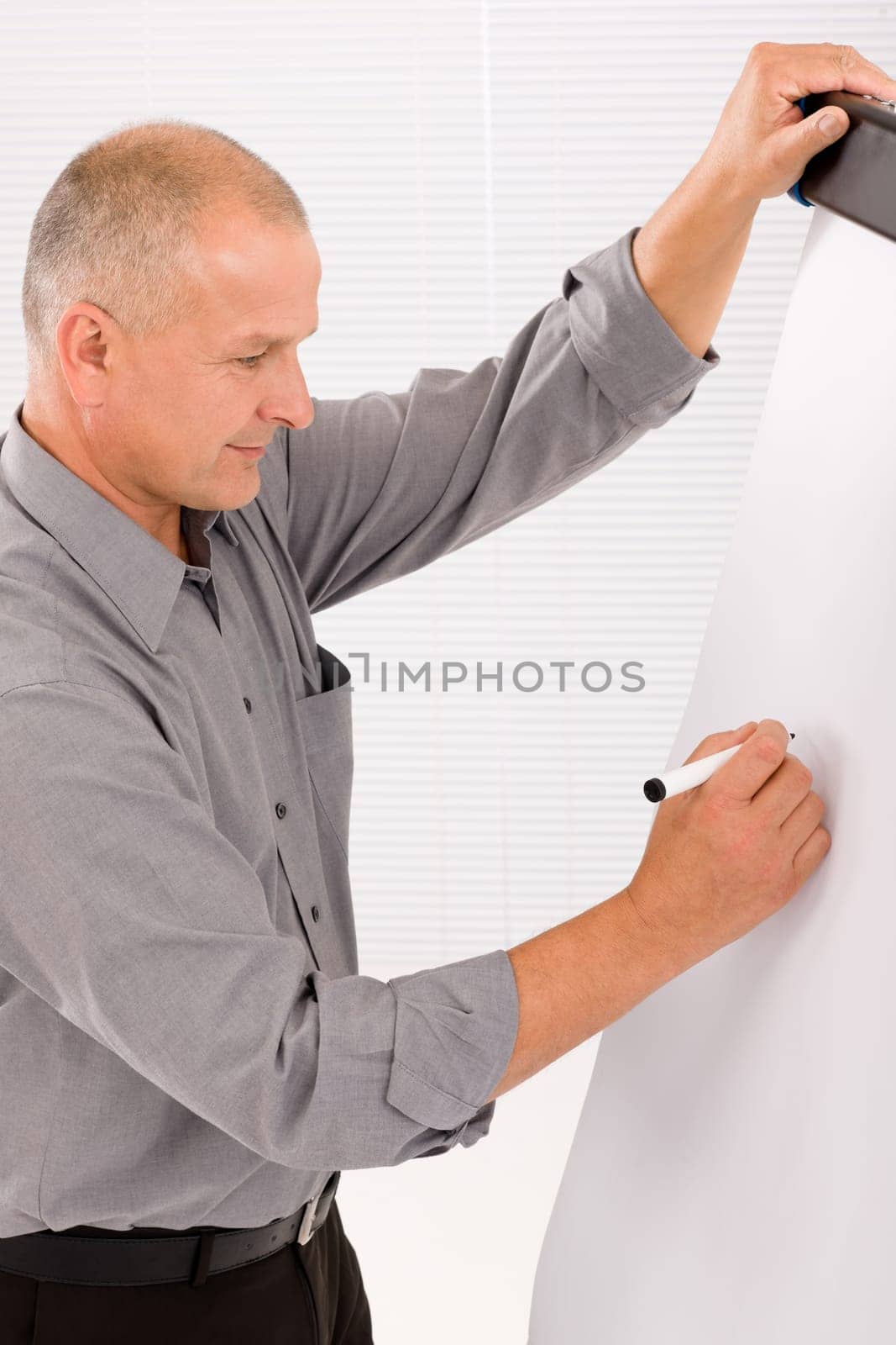 Handsome mature businessman writing at empty flip chart looking aside