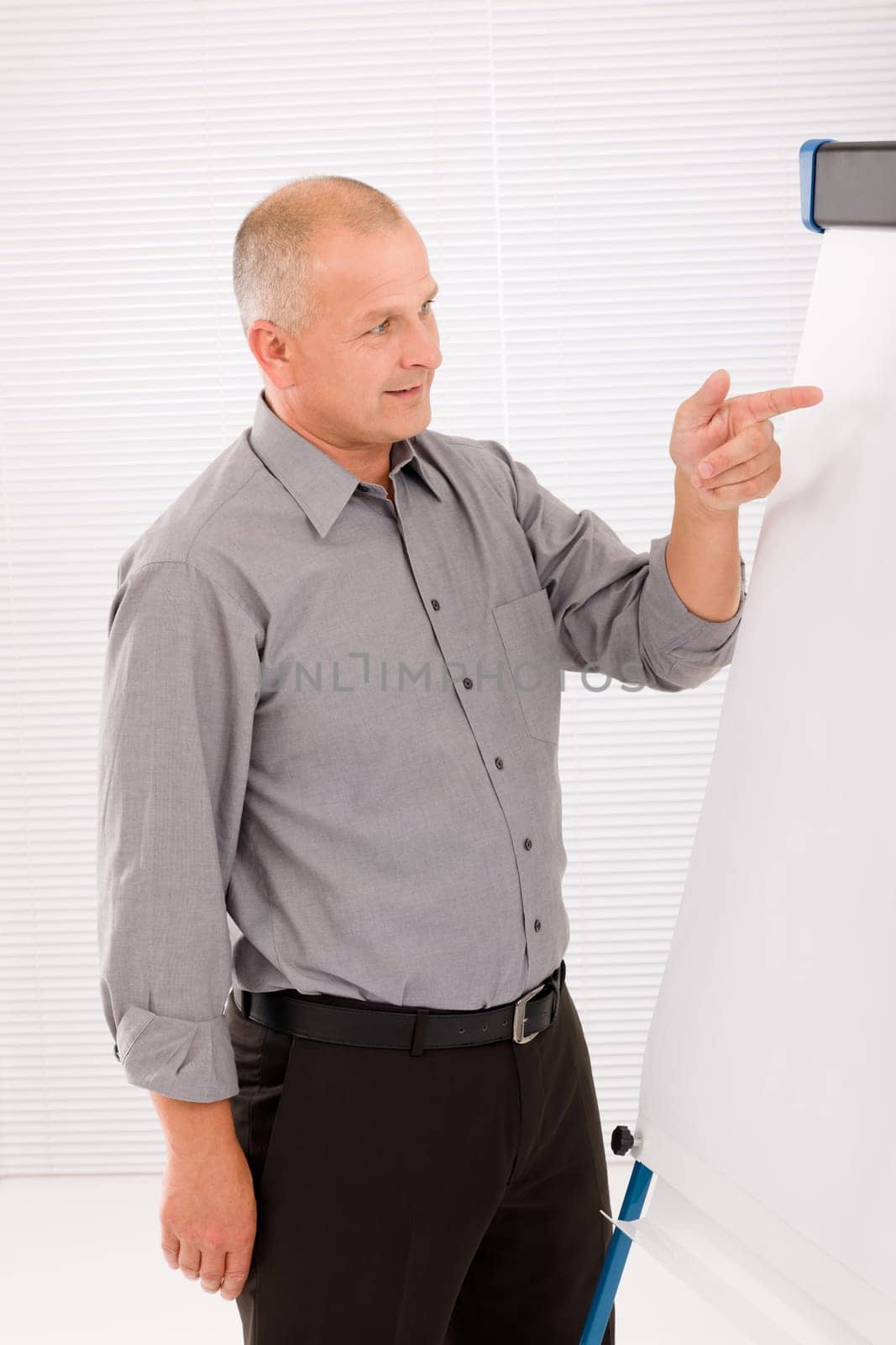 Mature handsome businessman pointing at empty flip chart looking aside
