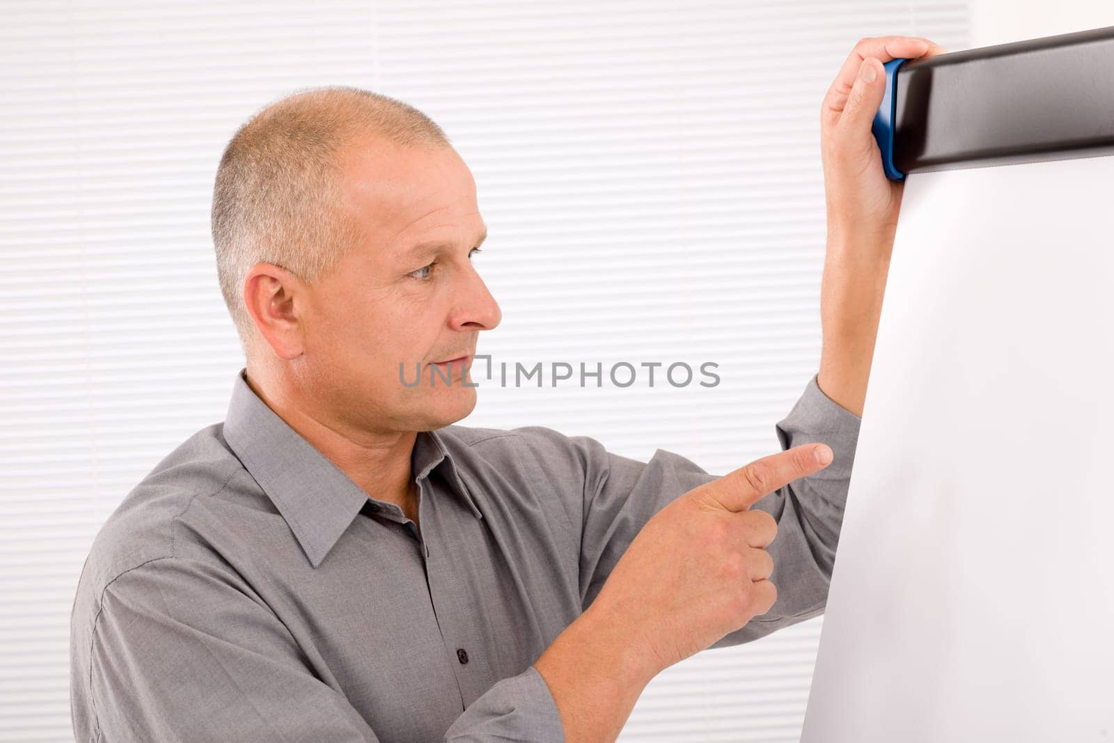 Mature handsome businessman pointing at empty flip chart looking aside