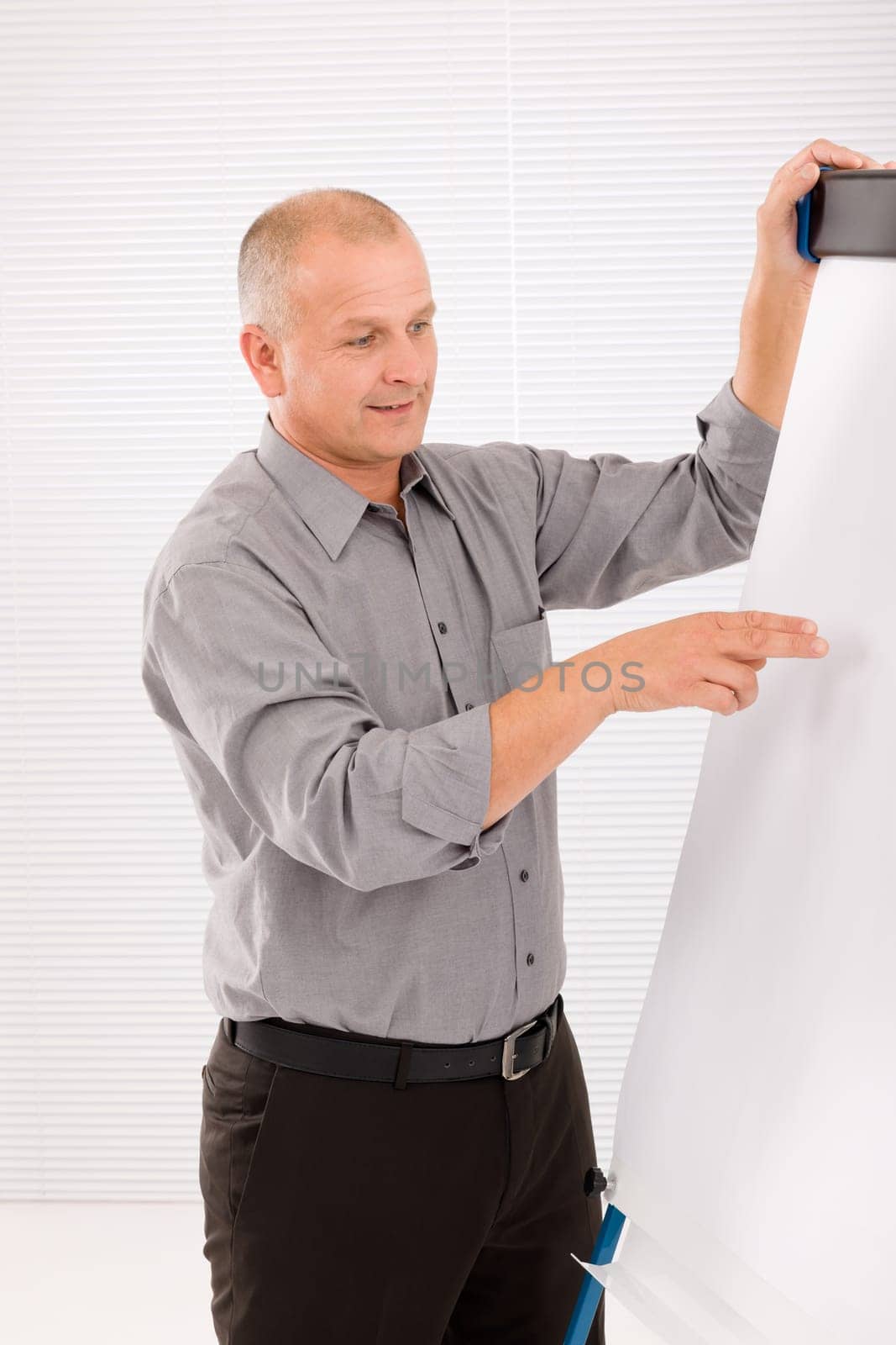 Mature handsome businessman pointing at empty flip chart looking aside