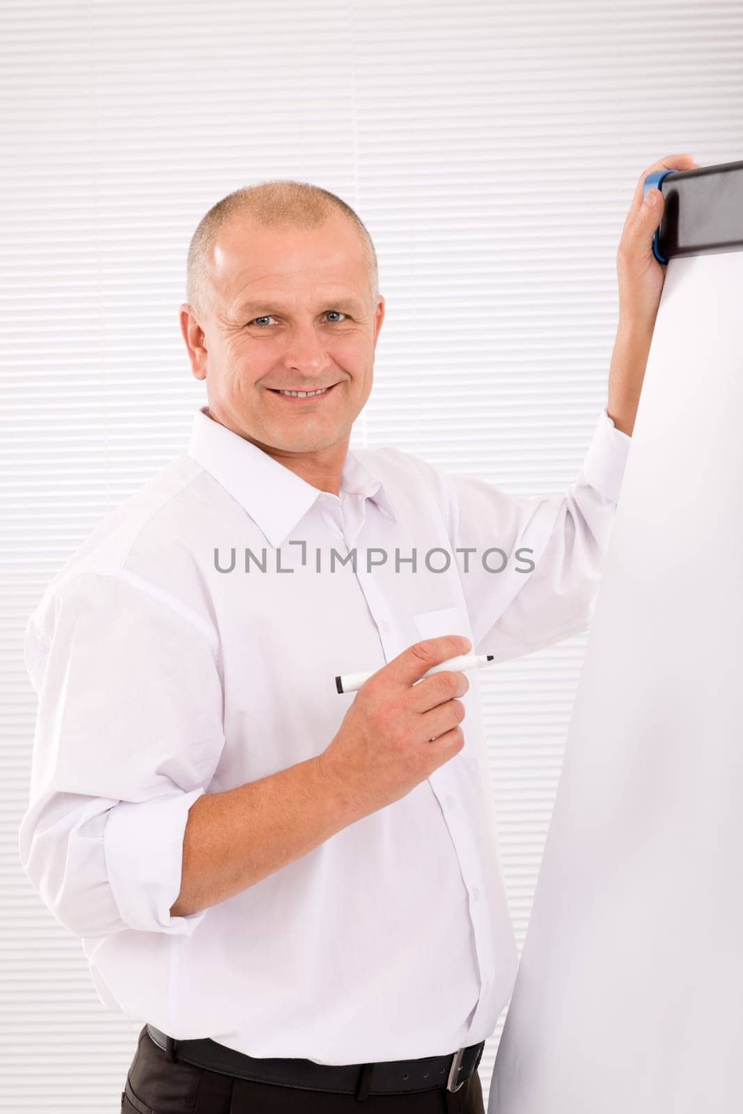 Handsome mature businessman writing at empty flip chart looking front