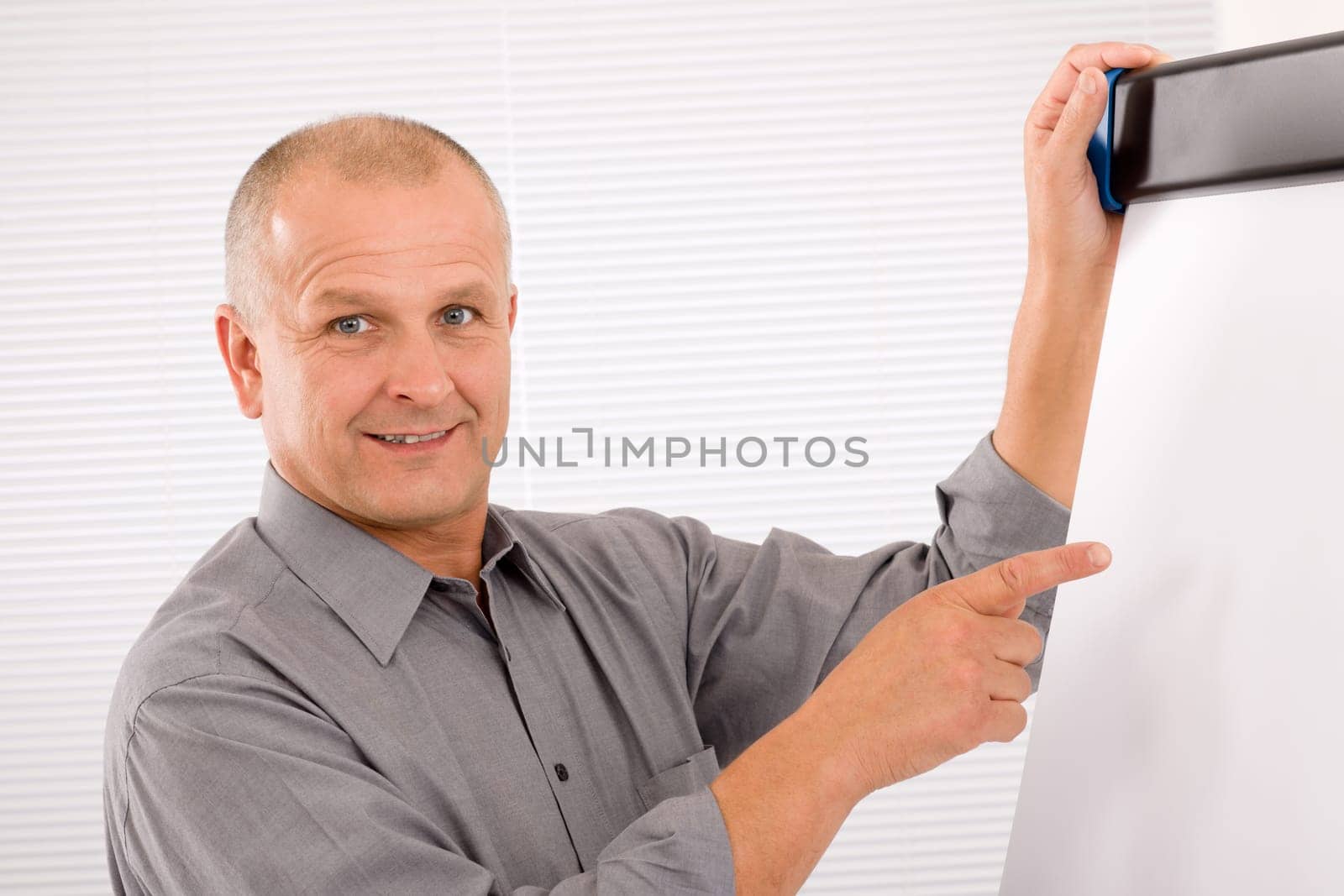 Mature handsome businessman pointing at empty flip chart looking aside