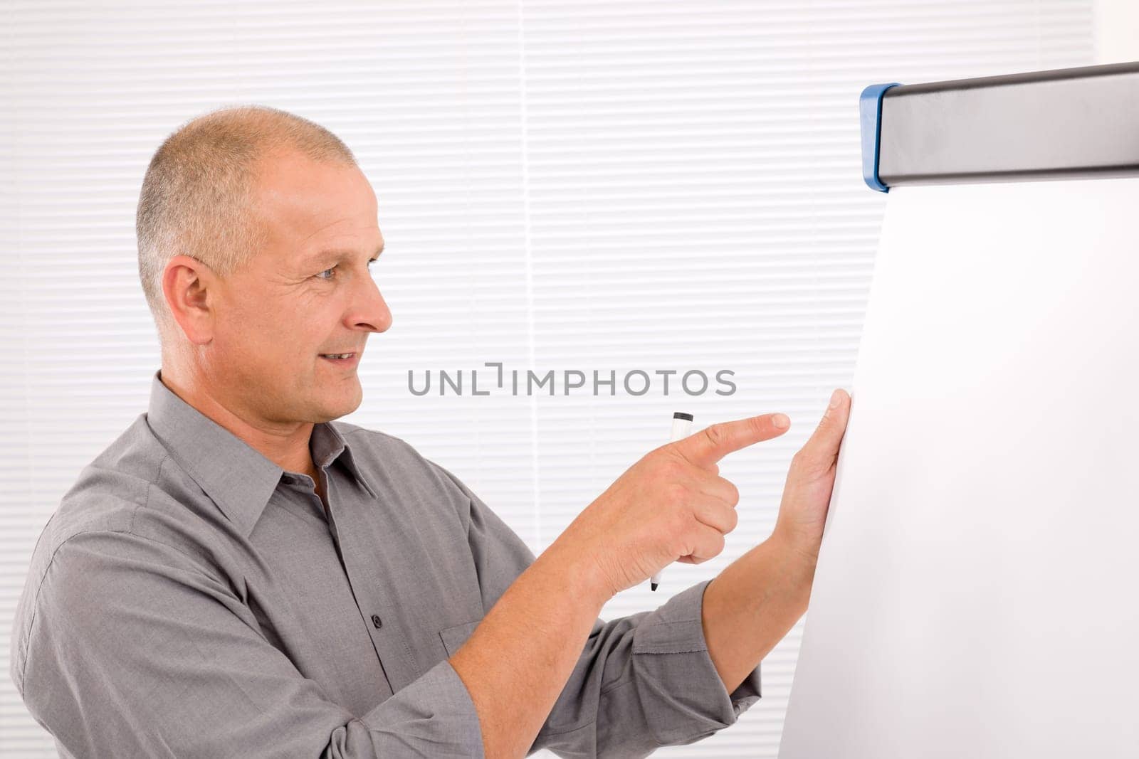 Handsome mature businessman writing at empty flip chart looking aside