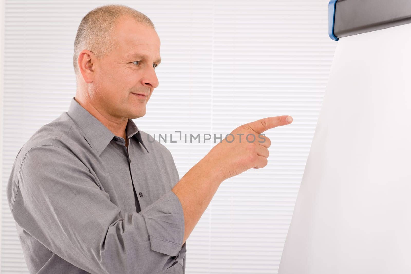 Mature handsome businessman pointing at empty flip chart looking aside