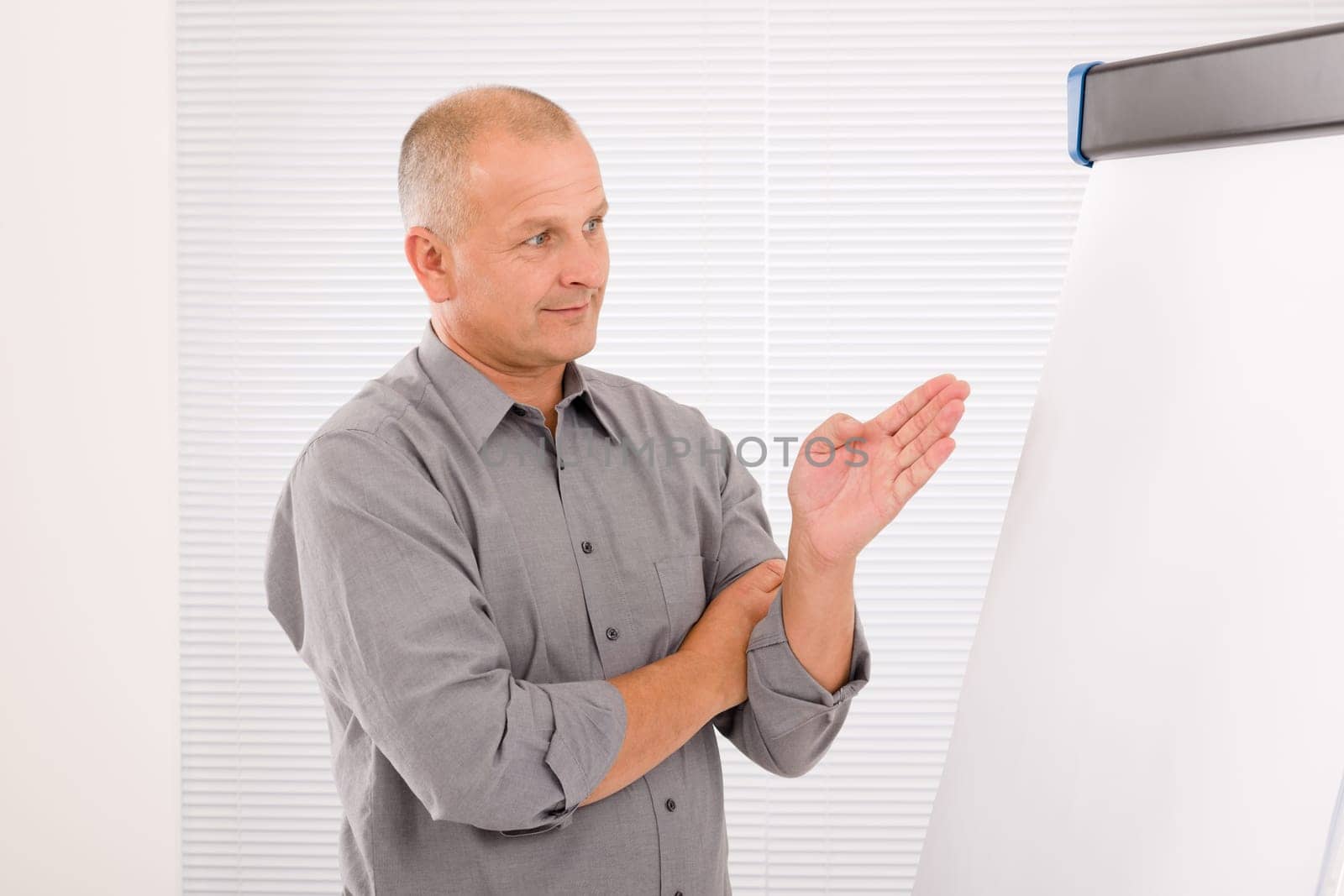 Mature handsome businessman pointing at empty flip chart looking aside