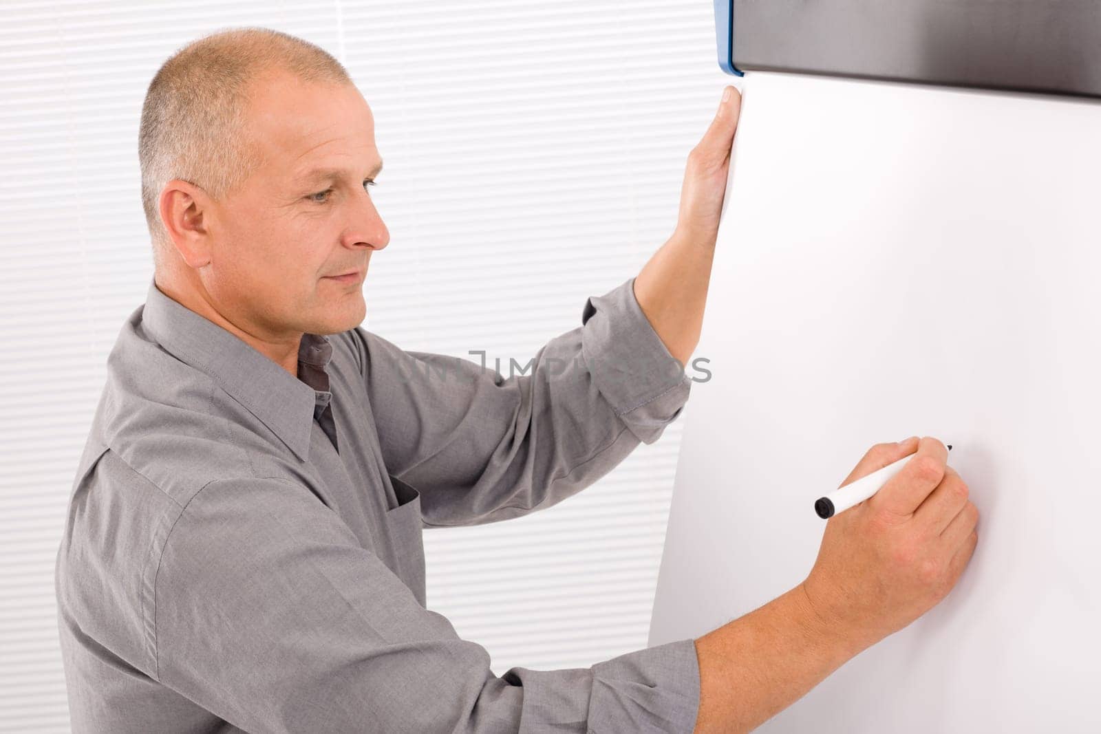 Handsome mature businessman writing at empty flip chart looking aside