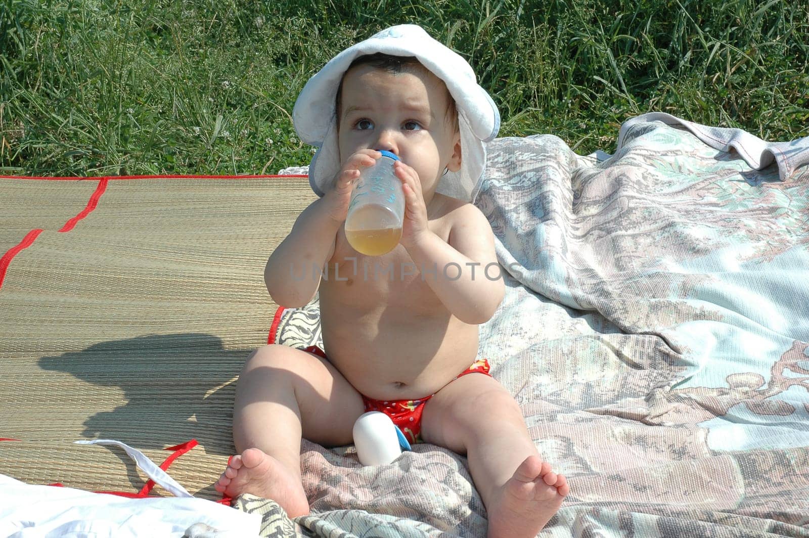 baby with a hat and bottle in the beach