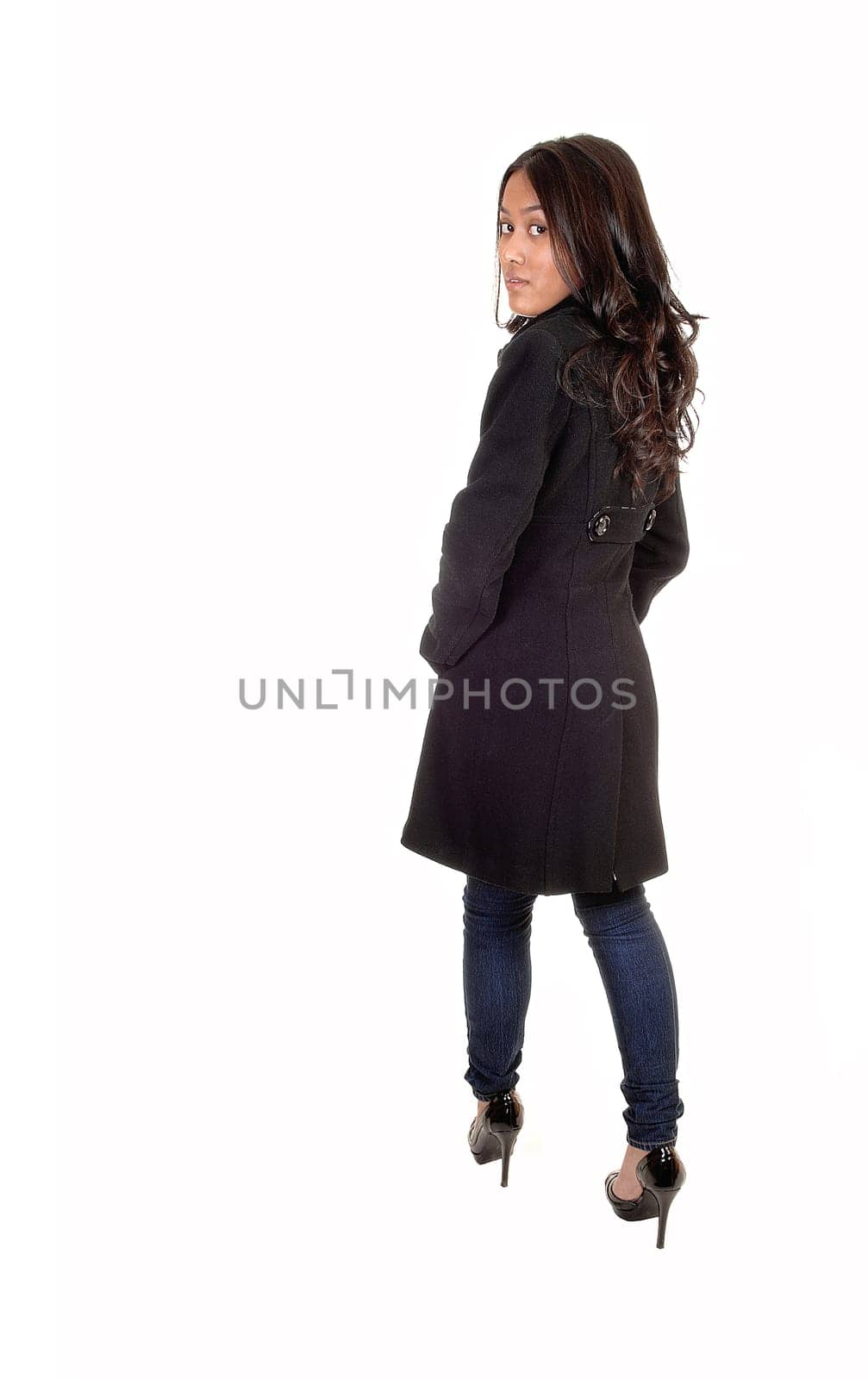 A young Asian woman in a gray winter coat and jeans standing and looking  over her shoulder with long brunette hair, for white background.