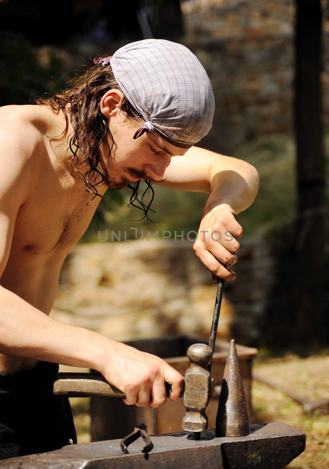 Young blacksmith hammering hot iron on anvil