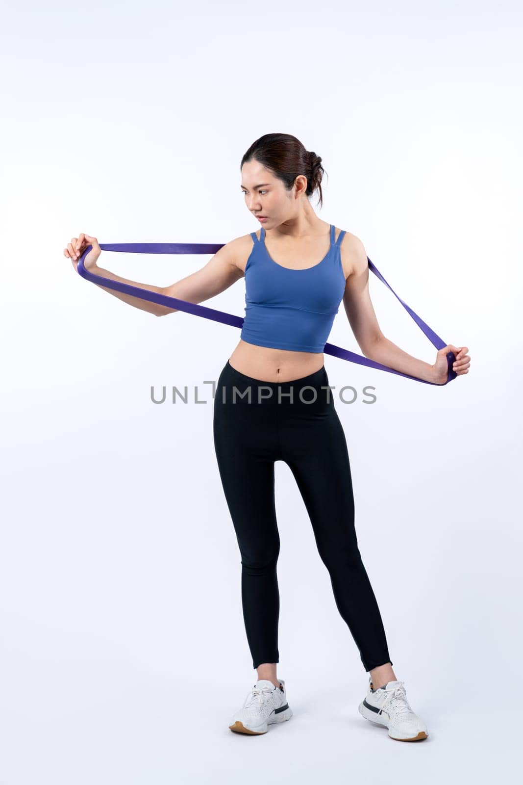 Vigorous energetic woman in sportswear portrait stretching resistance sport band. Young athletic asian woman strength and endurance training session workout routine concept on isolated background.