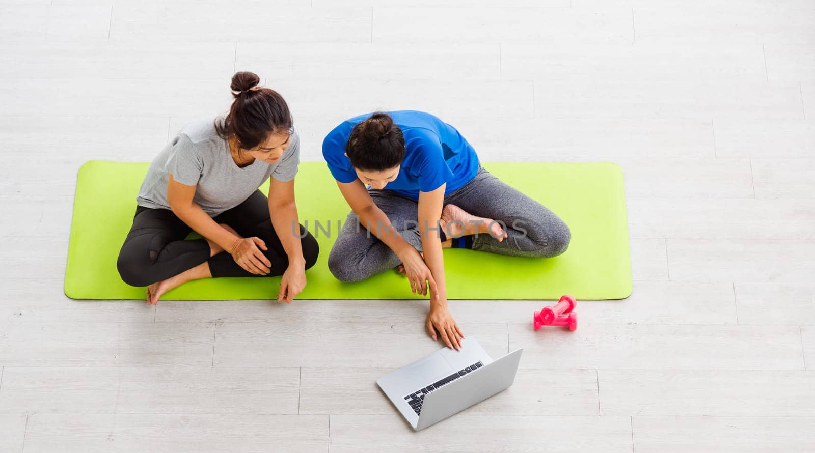 Overhead two Asian lifestyle adult and young woman in sportswear sitting floor on mat with dumbbells look laptop computer for training videos online in yoga studio, fit sport healthy workout exercise