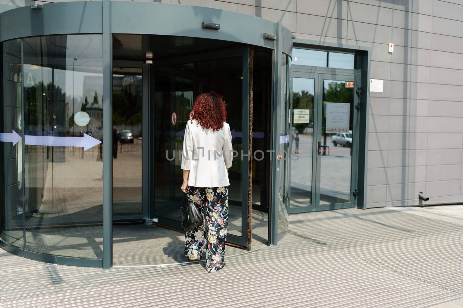 Portrait woman entering a supermarket. Caucasian model with long dark hair, wearing a white jacket and colored trousers. by Matiunina