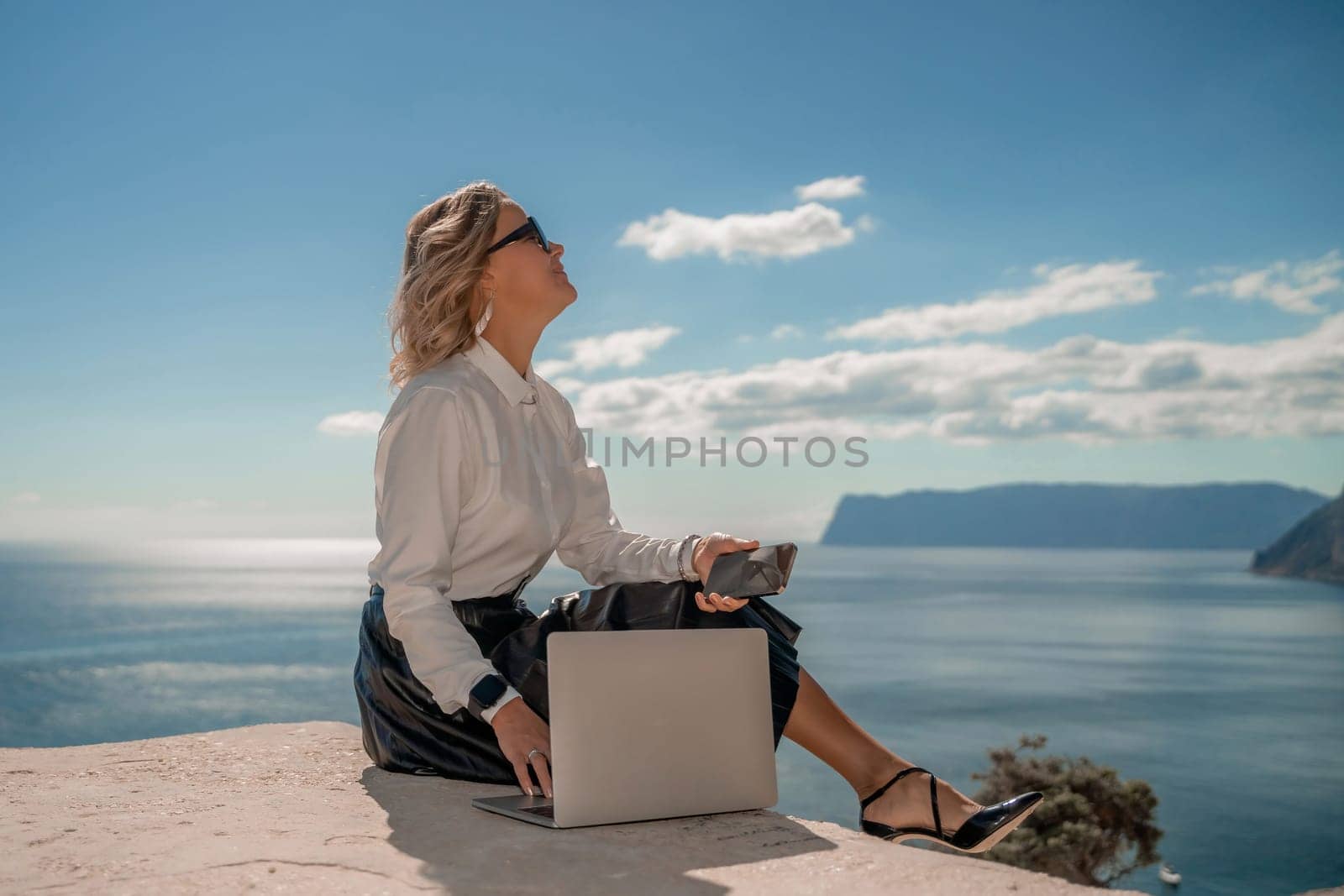 Freelance women sea working on a computer. Pretty middle aged woman with computer and phone outdoors with beautiful sea view. The concept of remote work