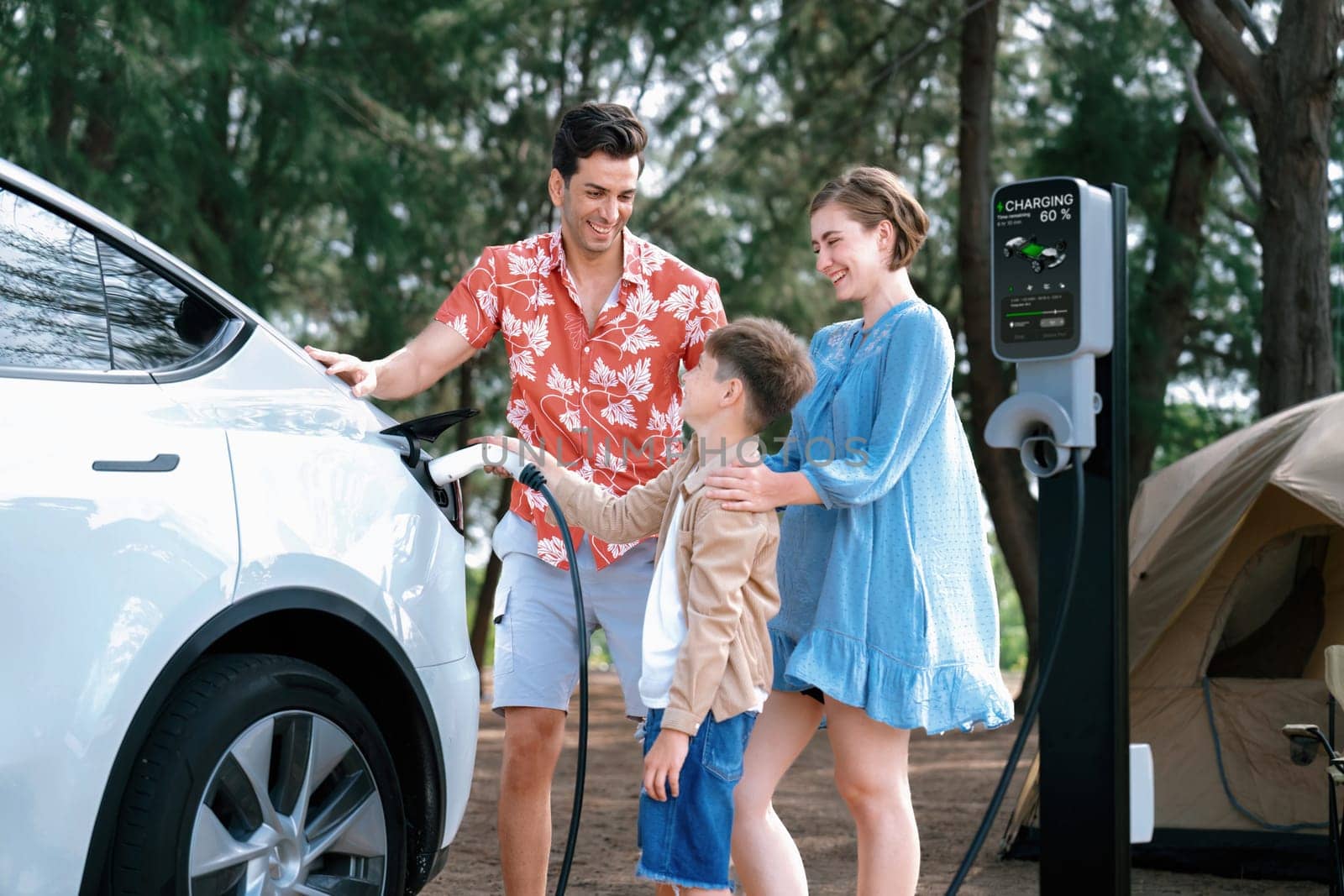 Outdoor adventure and family vacation camping in nature travel by eco friendly car for sustainable future. Lovely family recharge EV car with EV charging station in campsite. Perpetual