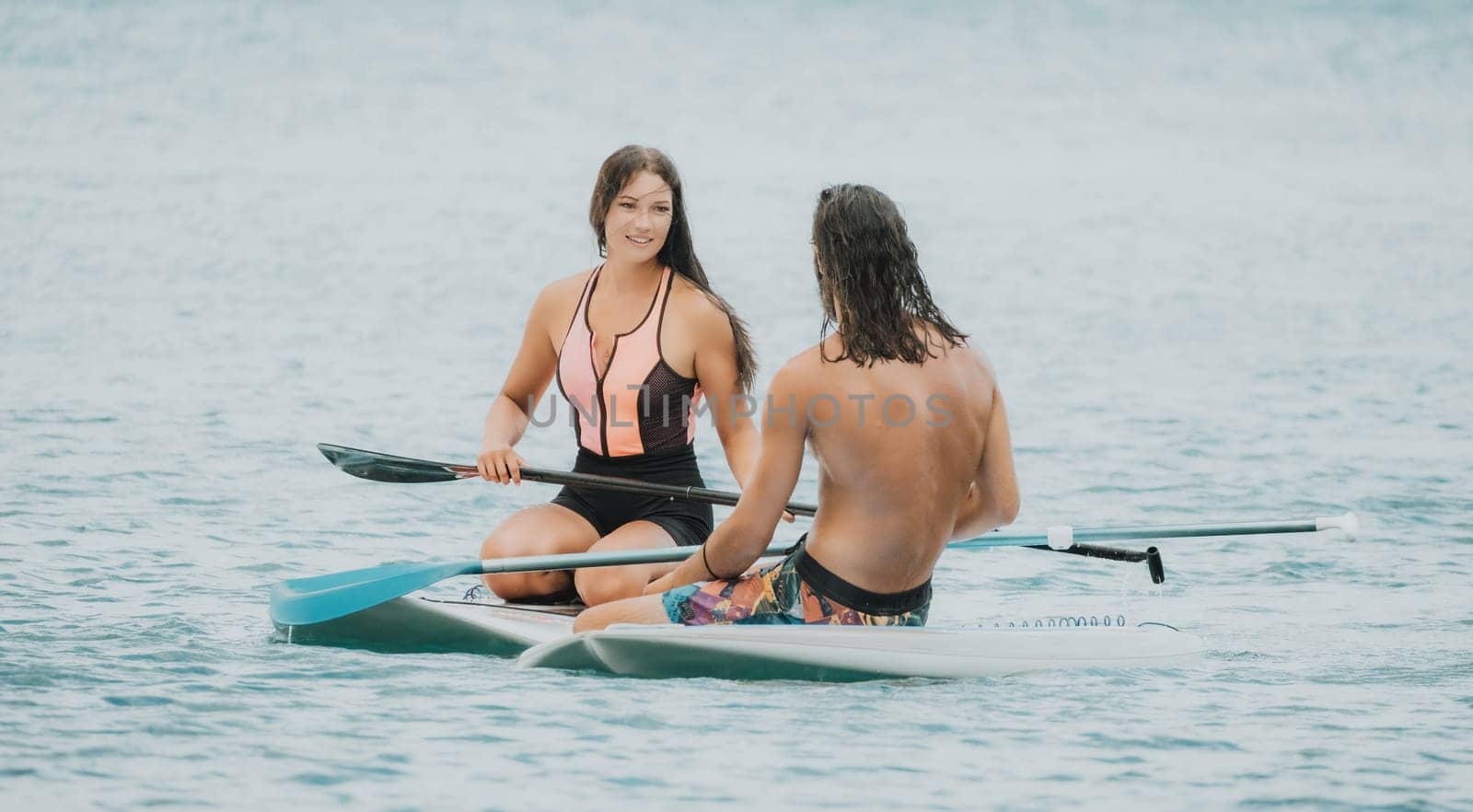 Sea woman and man on sup. Silhouette of happy young woman and man, surfing on SUP board, confident paddling through water surface. Idyllic sunset. Active lifestyle at sea or river