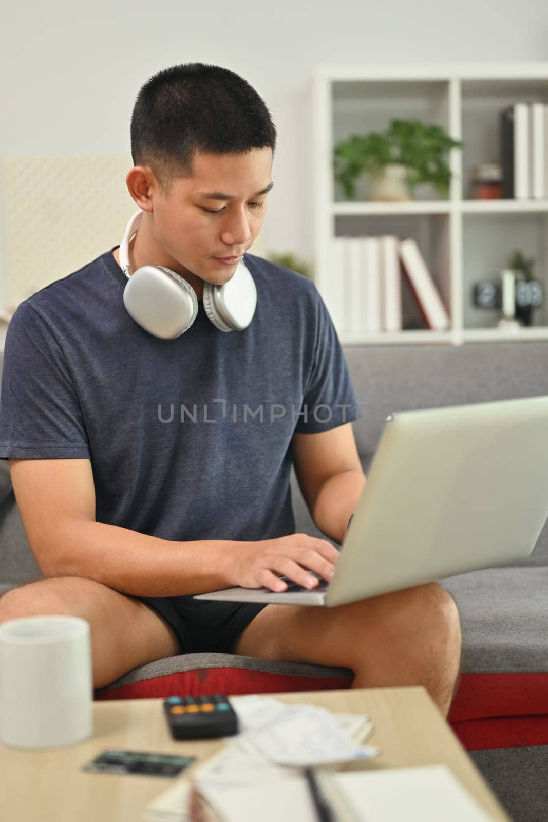 Concentrated male freelancer working online or browsing web on laptop at home by prathanchorruangsak