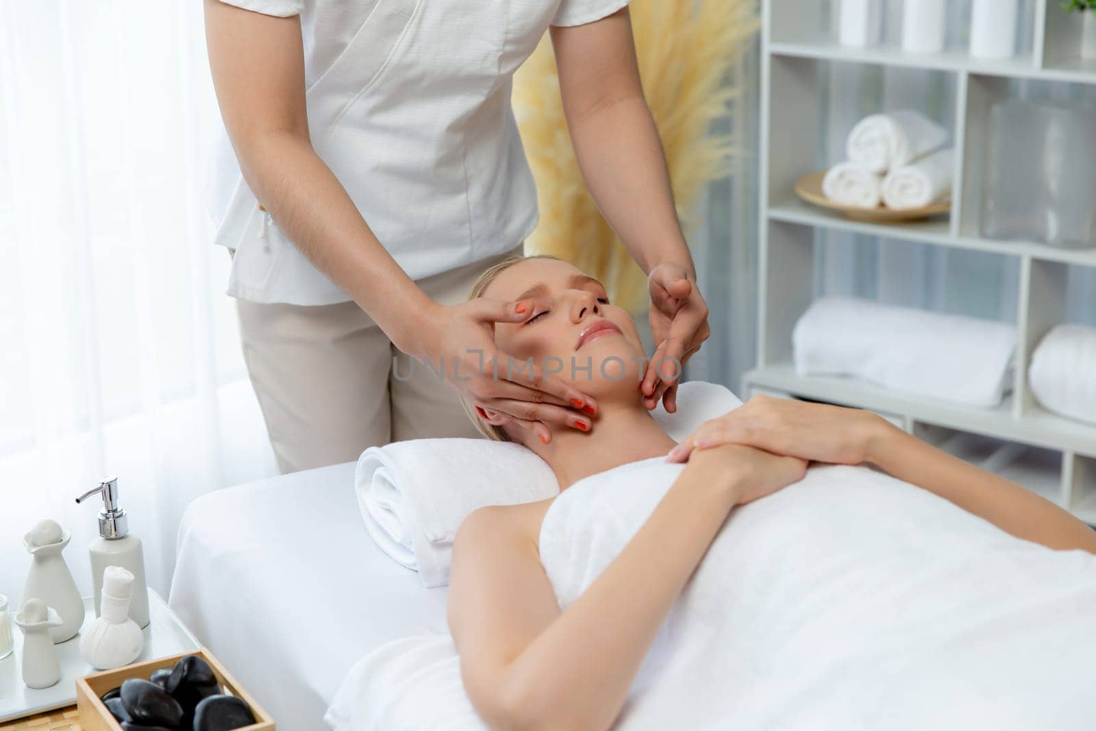 Caucasian woman enjoying relaxing anti-stress head massage and pampering facial beauty skin recreation leisure in dayspa modern light ambient at luxury resort or hotel spa salon. Quiescent