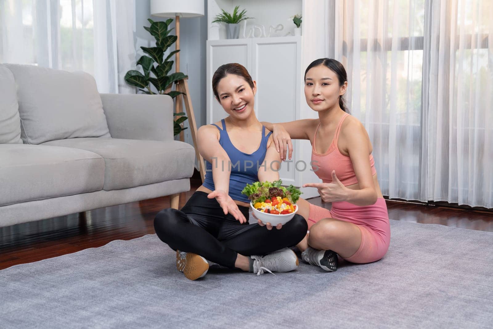 Young sporty Asian women in sportswear holding salad bowl together. Vigorous by biancoblue