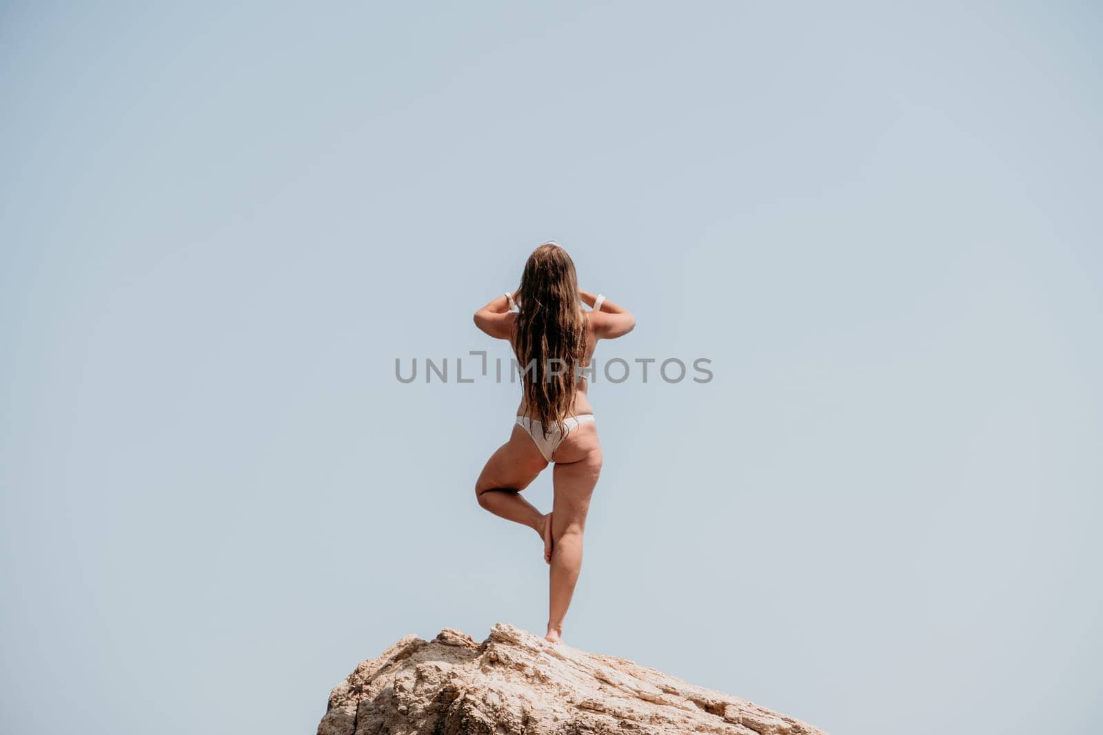 Woman meditating in yoga pose silhouette at the ocean, beach and rock mountains. Motivation and inspirational fit and exercising. Healthy lifestyle outdoors in nature, fitness concept.