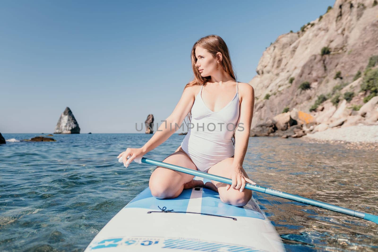 Close up shot of happy young caucasian woman looking at camera and smiling. Cute woman portrait in bikini posing on a volcanic rock high above the sea