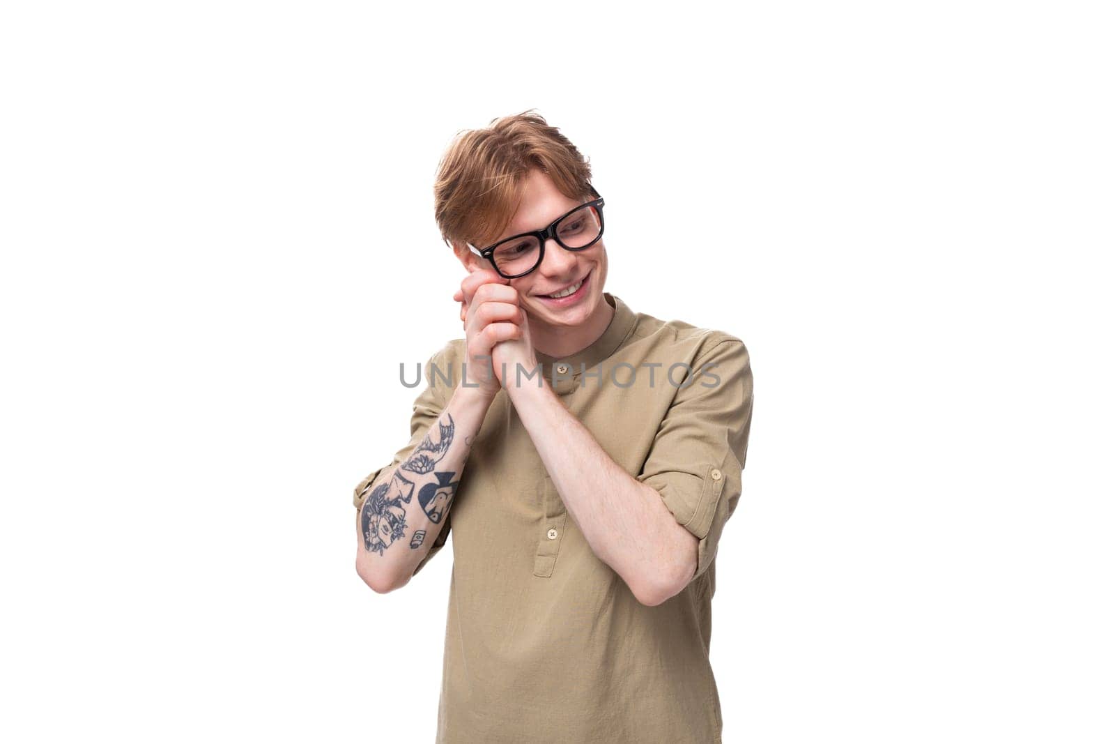 smart young red-haired man in a beige shirt wears eyeglasses on a white background.