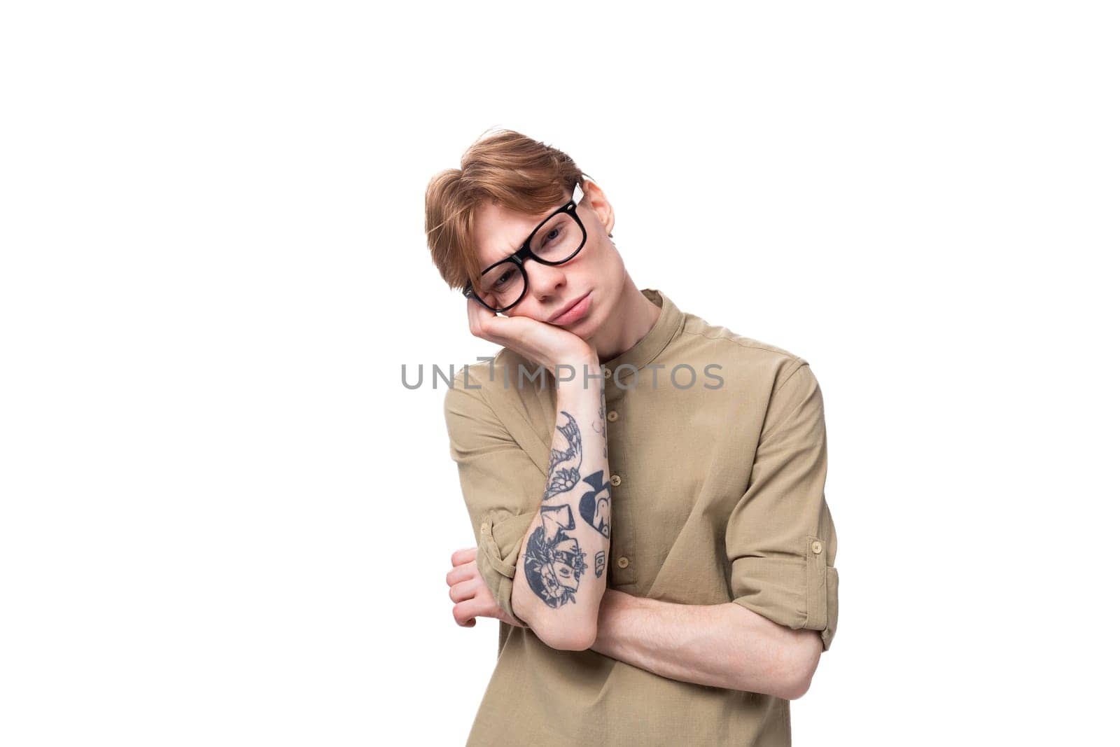 young sad red-haired european man dressed in a light brown shirt with a tattoo on his arm feels tired.
