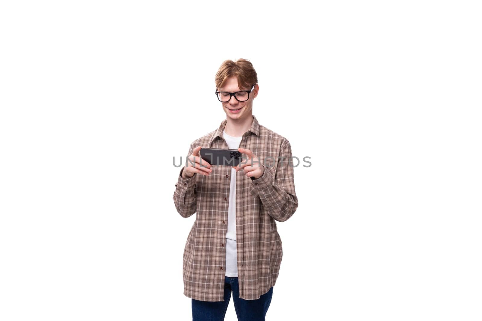 cute caucasian student guy in glasses plays a game on the phone.