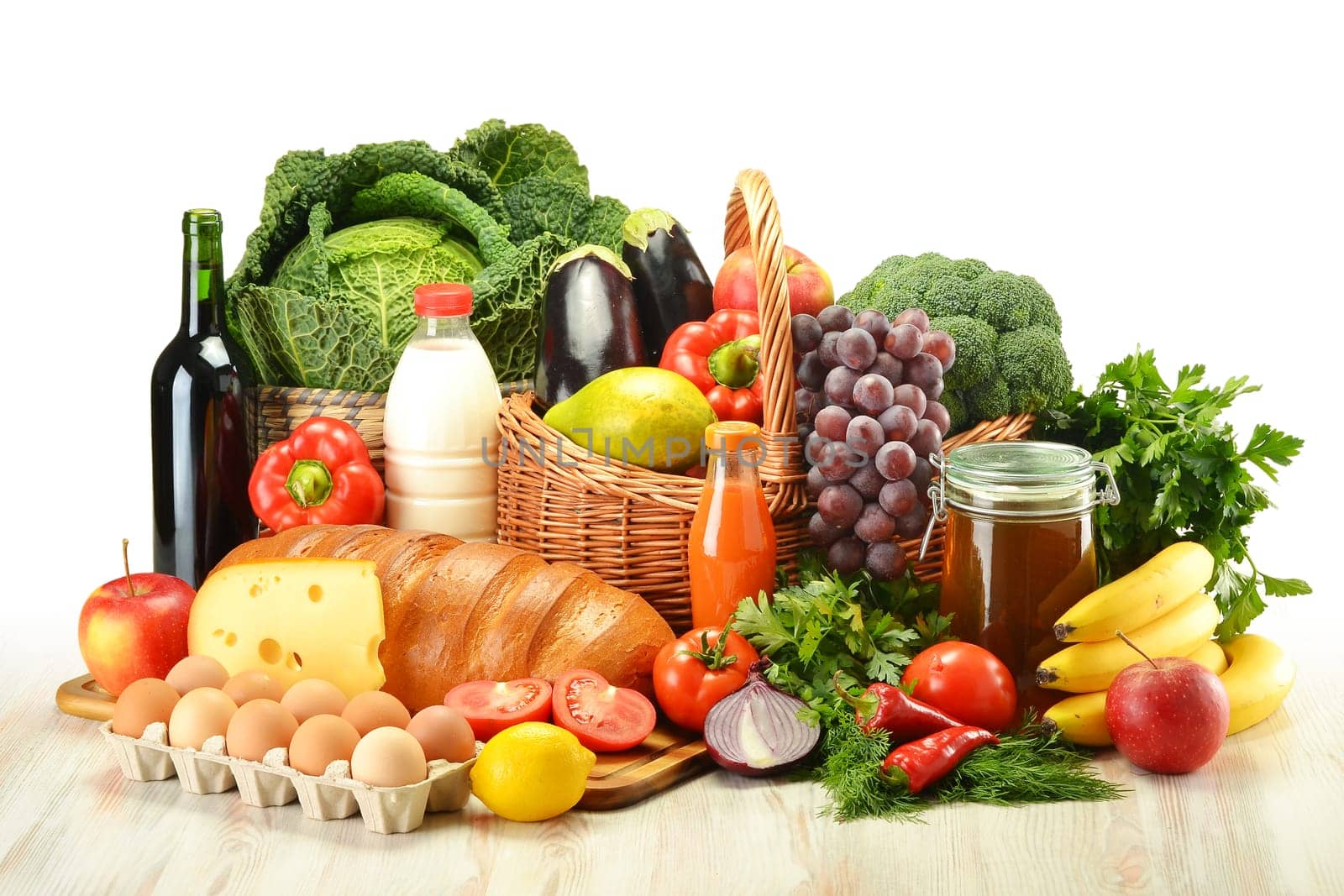 Groceries in wicker basket including vegetables, fruits, bakery and dairy products and wine isolated on white