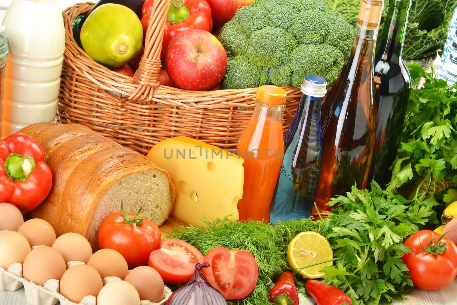 Groceries in wicker basket including vegetables, fruits, bakery and dairy products and wine isolated on white