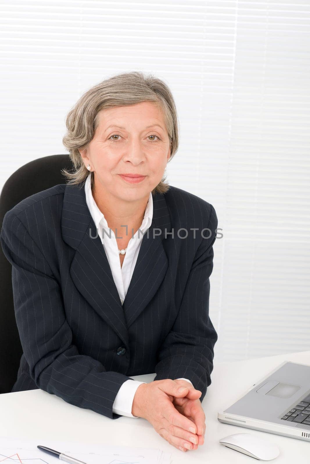 Successful senior businesswoman sitting behind office table with laptop portrait