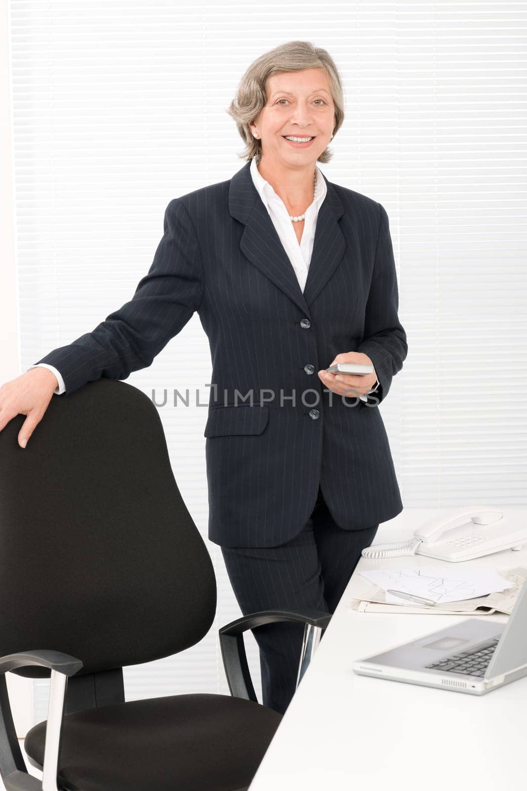 Smiling successful senior businesswoman standing behind office table portrait