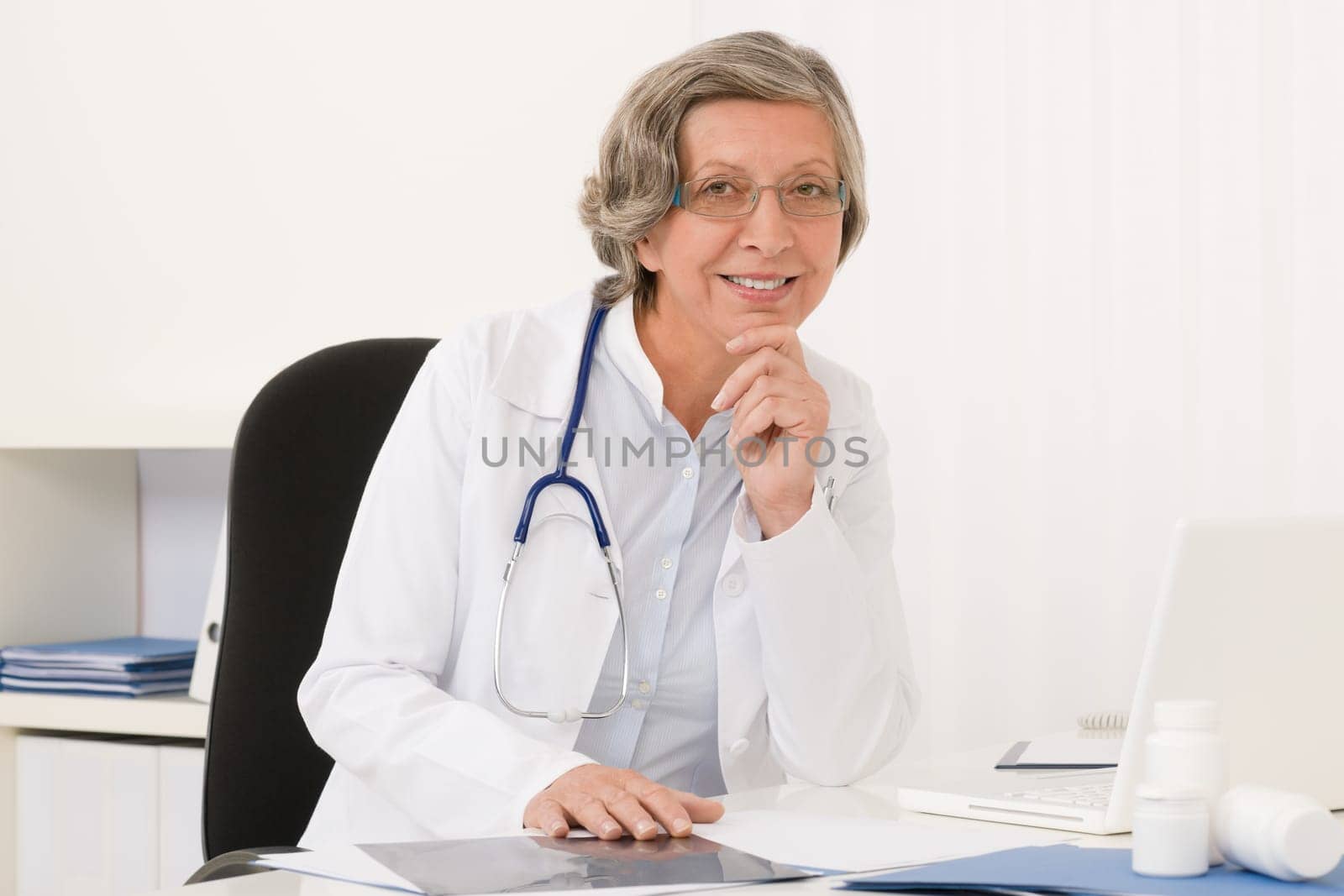 Doctor office - senior female physician sit behind desk smiling