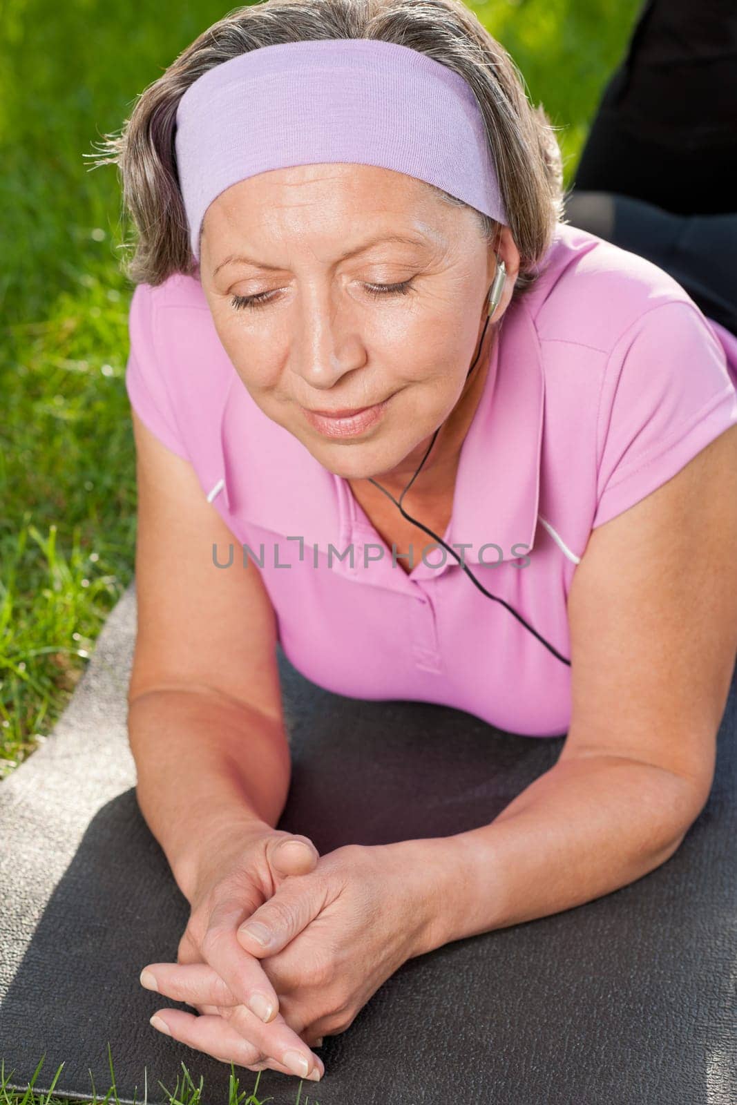 Senior sportive woman on mat listen music outside sunny day