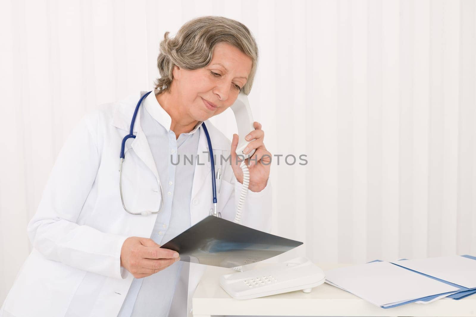 Senior doctor female on phone watch down x-ray at office