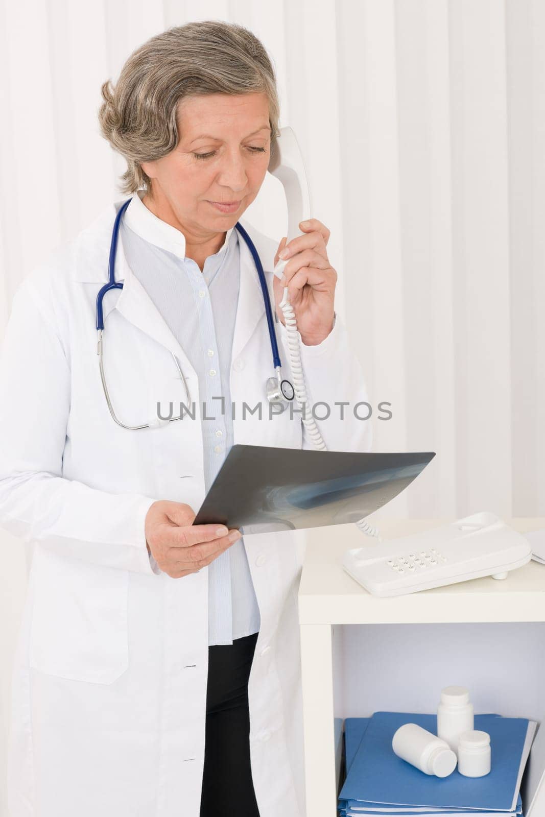 Senior doctor female on phone watch down x-ray at office