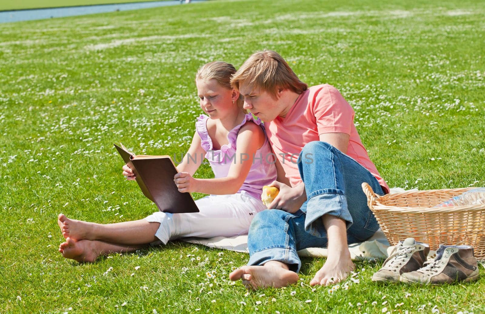 Teenager siblings reading book at picnic in the park in a bright sunny day