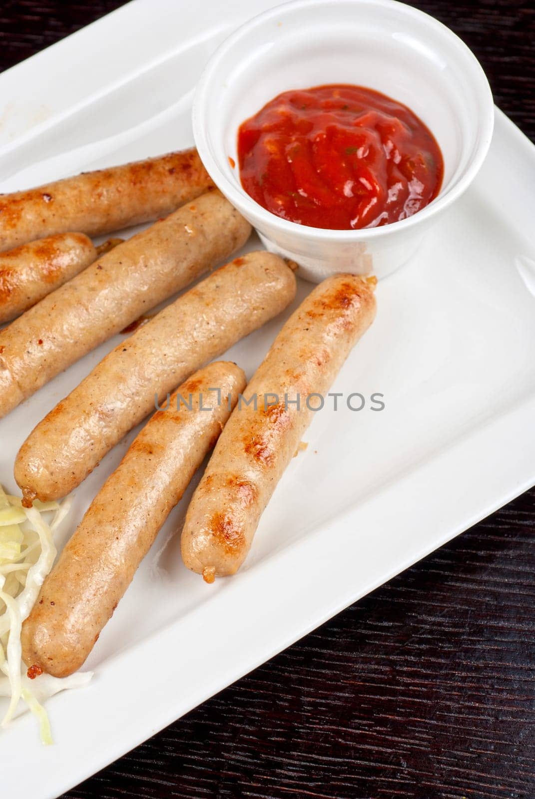 Grilled sausages with cabbage, greens and tomato sauce on white plate