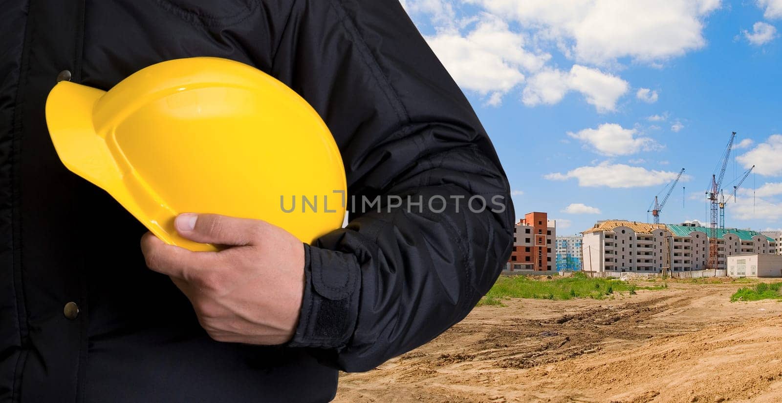 Closeup of yellow helmet at builder hands on building background