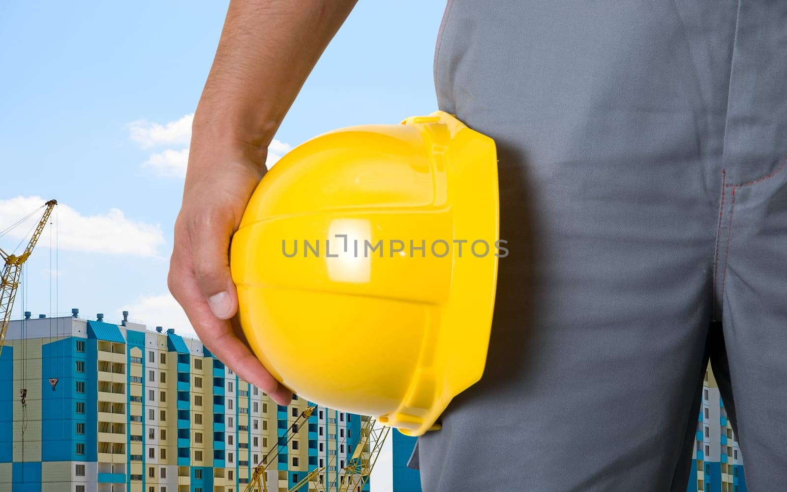 Closeup of yellow helmet at builder hands on building background