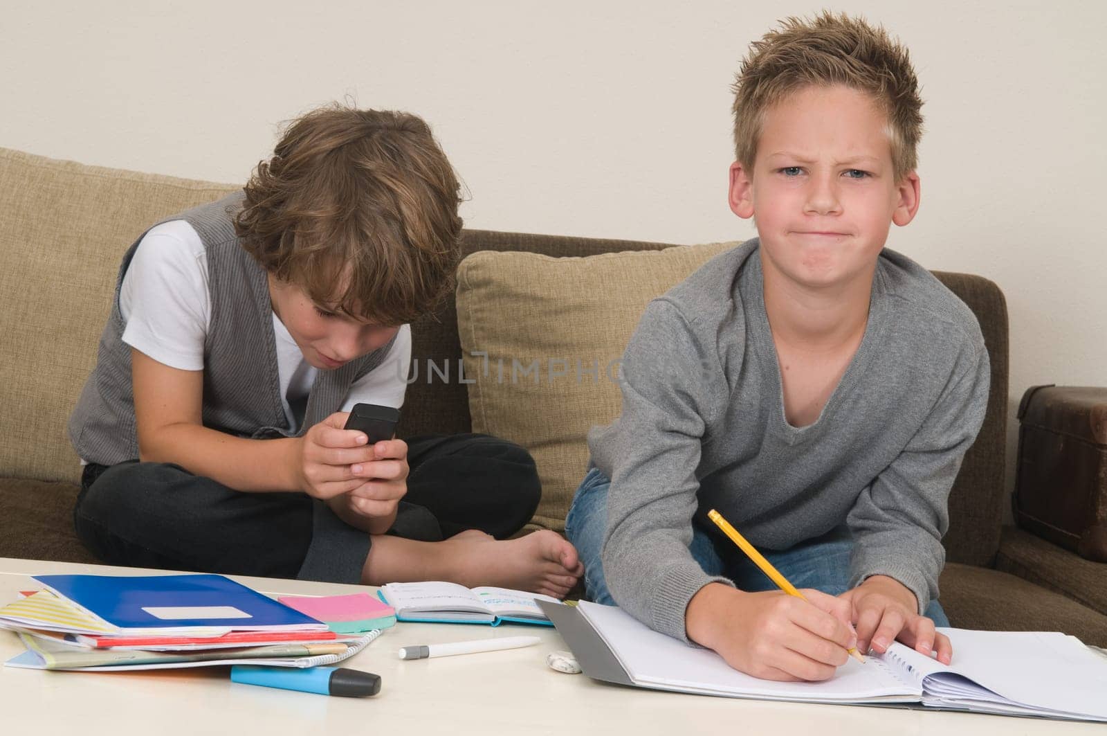 Two friends doing their homework in the livingroom. One of them is gaming, the other one is not ready and is jealous.
