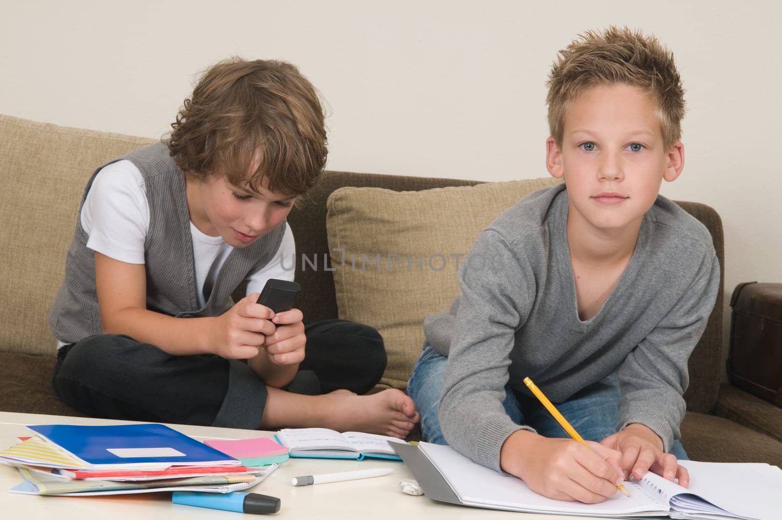 Two friends doing their homework in the livingroom. One of them is gaming, the other one is not ready and is jealous.