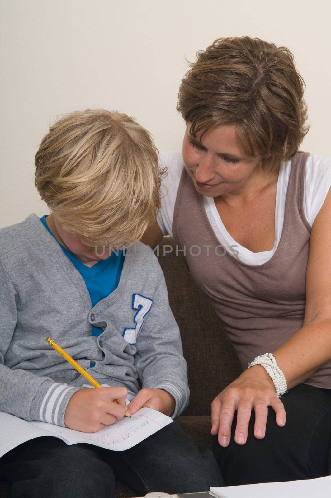 Boy is doing his homework in the livingroom while mother is helping him