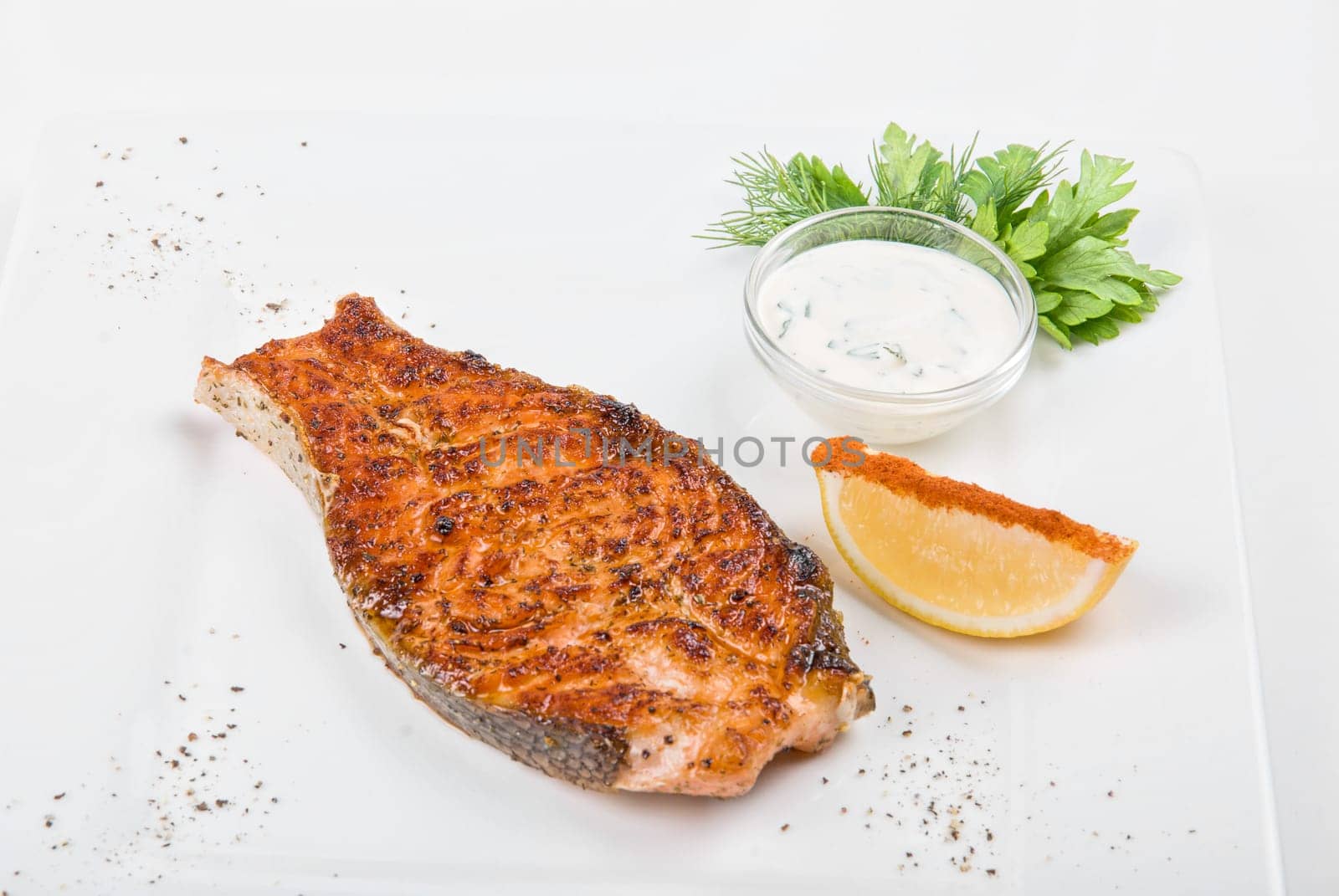 Grilled fish with sauce, lemon and greens on white plate