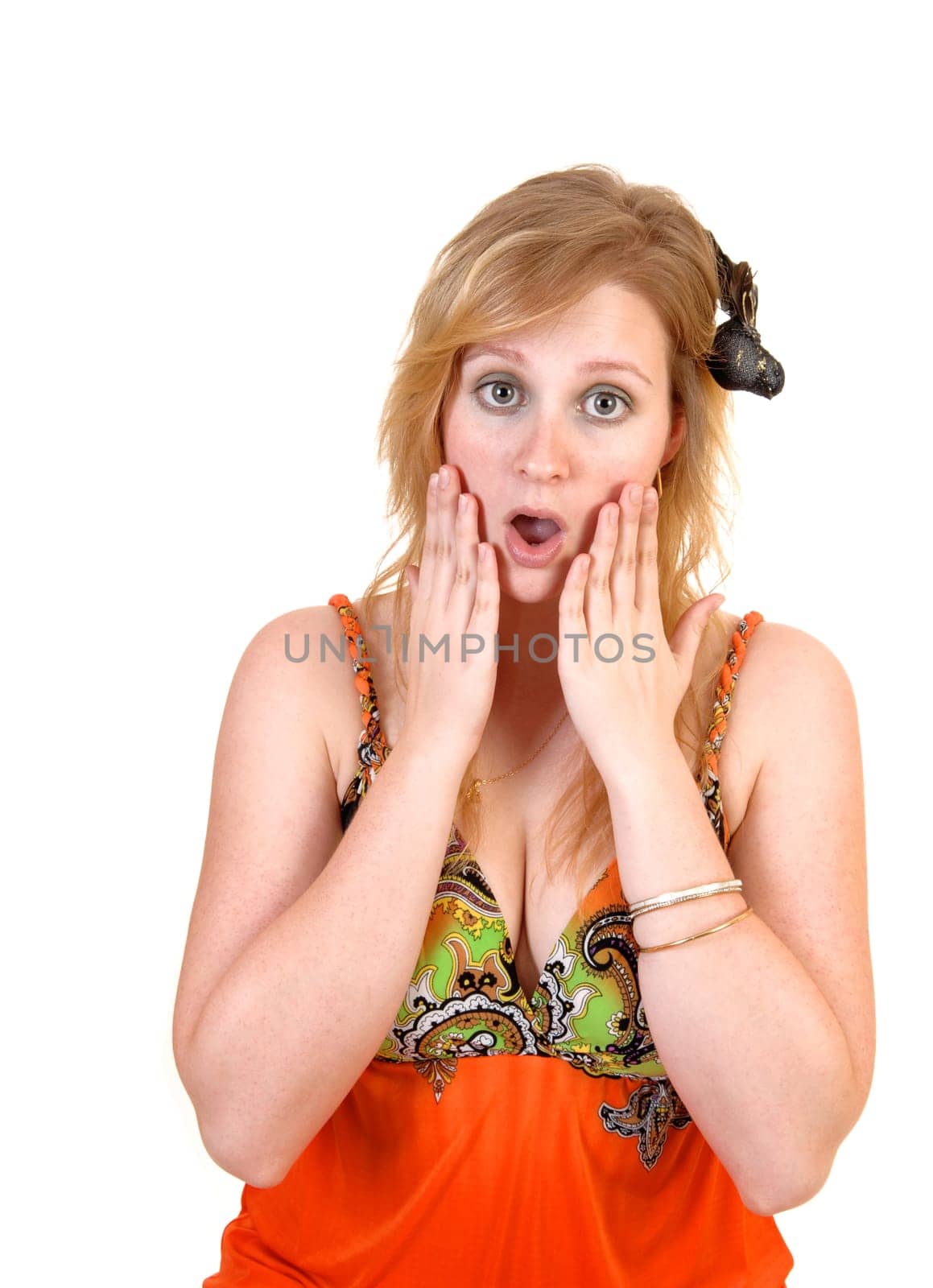 A shocked and surprised teenager girl, with a black bird in her blond hair holding her hands on her chick and mouth and eyes wait open, over white.