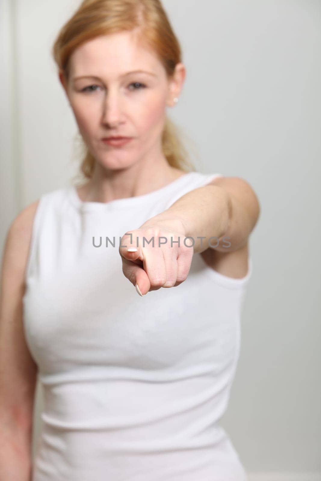Young woman pointing resolutely towards the camera. It can be seen blurred in the background.